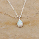 White Opal teardrop pendant sterling silver necklace on a beige stone background