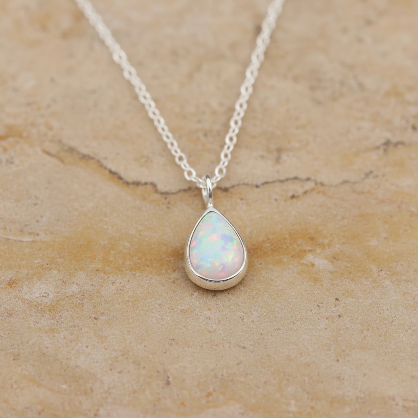 White Opal teardrop pendant sterling silver necklace on a beige stone background