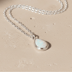 Necklace with a teardrop-shaped whiten opal pendant on a beige background