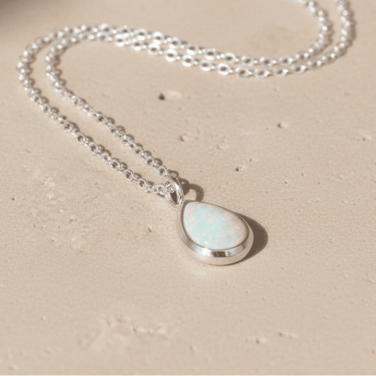 Necklace with a teardrop-shaped whiten opal pendant on a beige background
