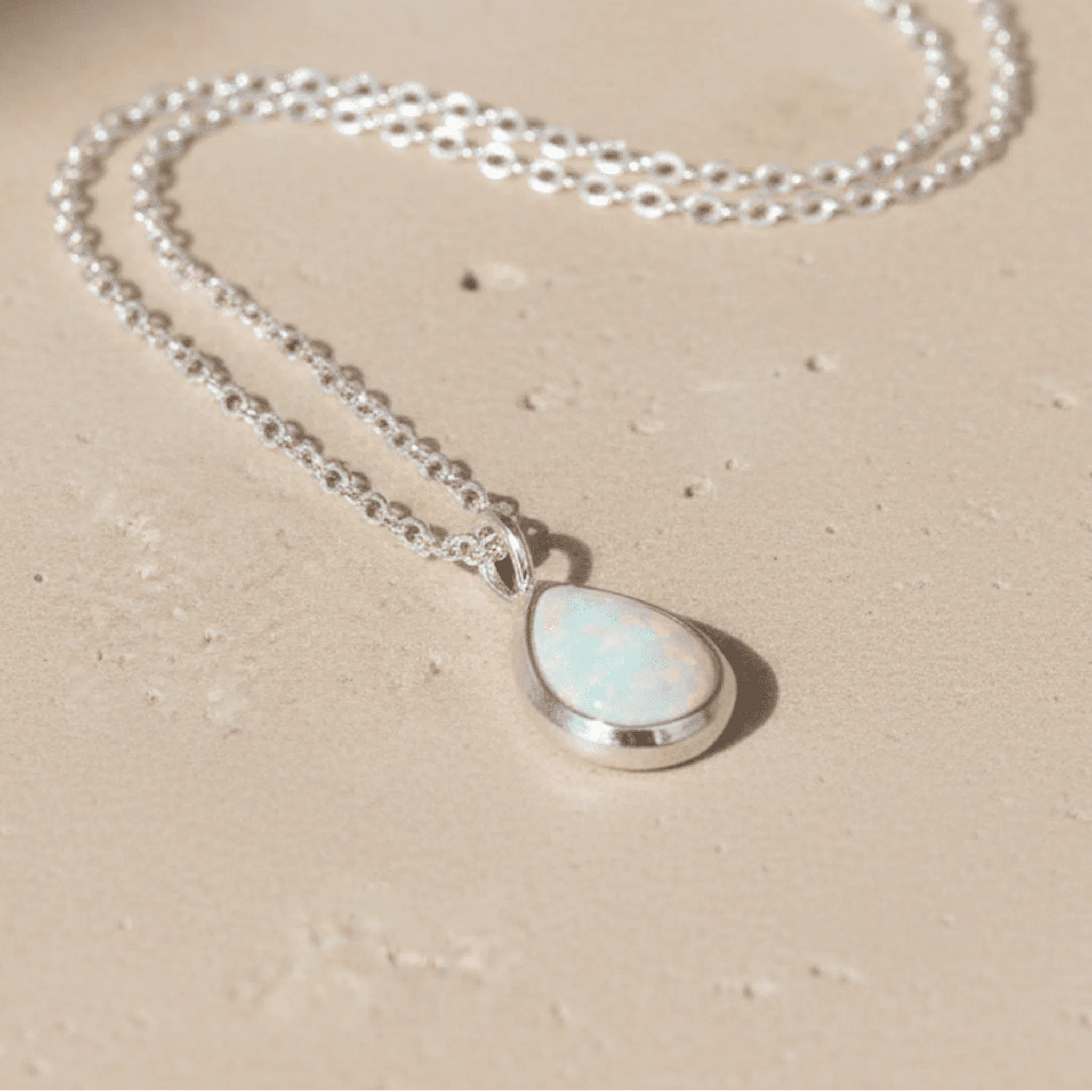 Necklace with a teardrop-shaped whiten opal pendant on a beige background