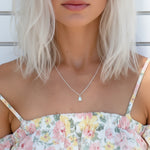 Woman wearing a floral dress and a dainty white opal silver necklace against a wooden background