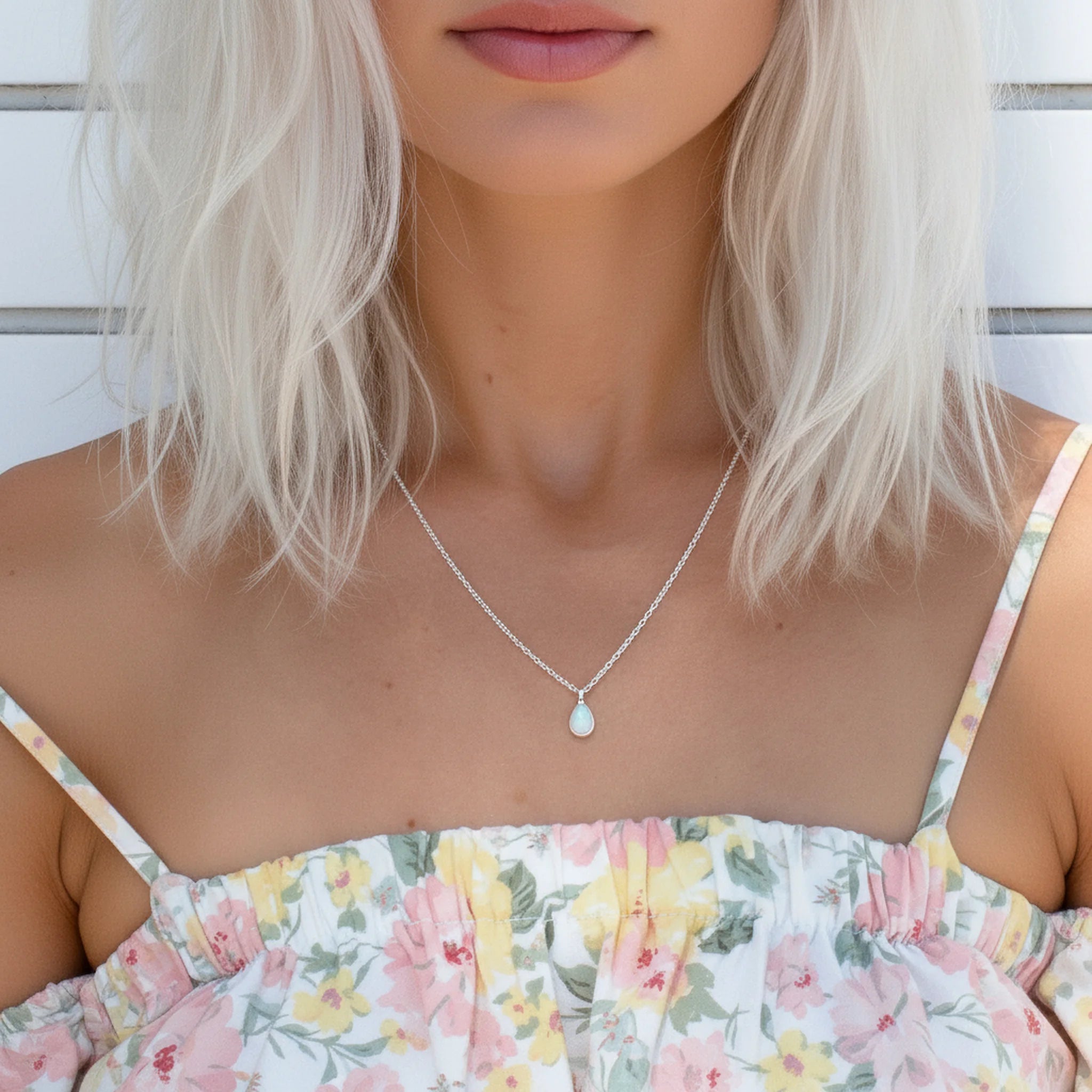 Woman wearing a floral dress and a dainty white opal silver necklace against a wooden background