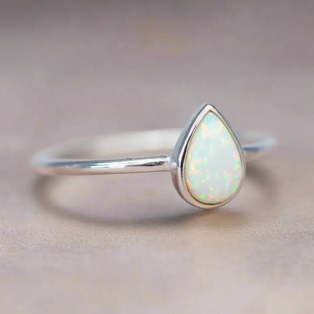 Silver ring with a teardrop-shaped white opal stone on a neutral background