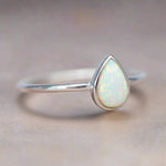 Silver ring with a teardrop-shaped white opal stone on a neutral background
