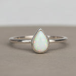 Silver ring with a teardrop-shaped opal stone on a textured surface.