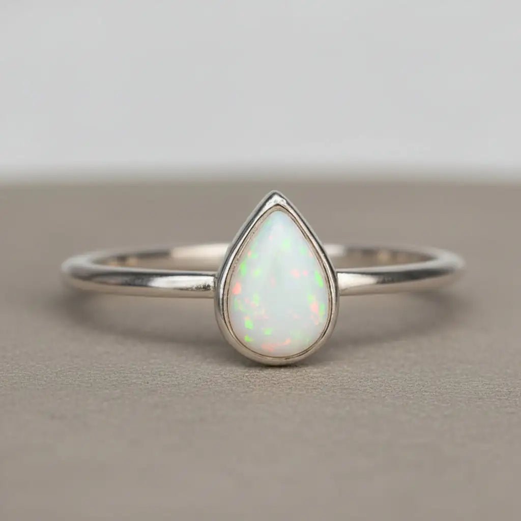 Sterling Silver ring with a teardrop-shaped white opal stone on a textured surface.