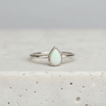 Silver ring with a teardrop-shaped opal stone on a light background