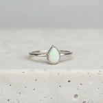 Silver ring with a teardrop-shaped opal stone on a light gray background