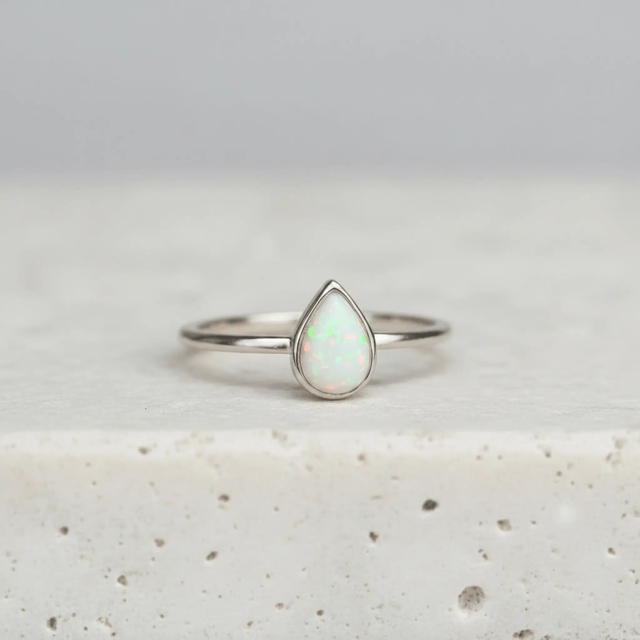 Silver ring with a teardrop-shaped opal stone on a light gray background