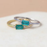 Two emerald-cut tourmaline gemstone rings in silver and gold on a textured beige surface