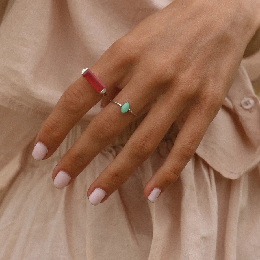 woman in a beige dress wearing two sterling silver rings, one with a large pink jade stone and the other with a small turquoise stone