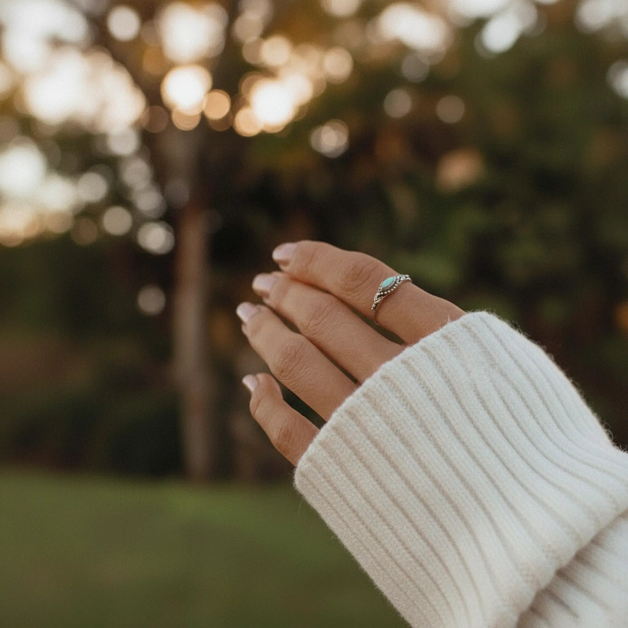 Hand wearing a dainty sterling silver turquoise ring with a blurred natural background