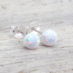 white Opal ball stud earrings on a light wooden background