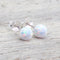 white Opal ball stud earrings on a light wooden background