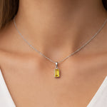 Necklace with a yellow gemstone pendant on a person wearing a white top.