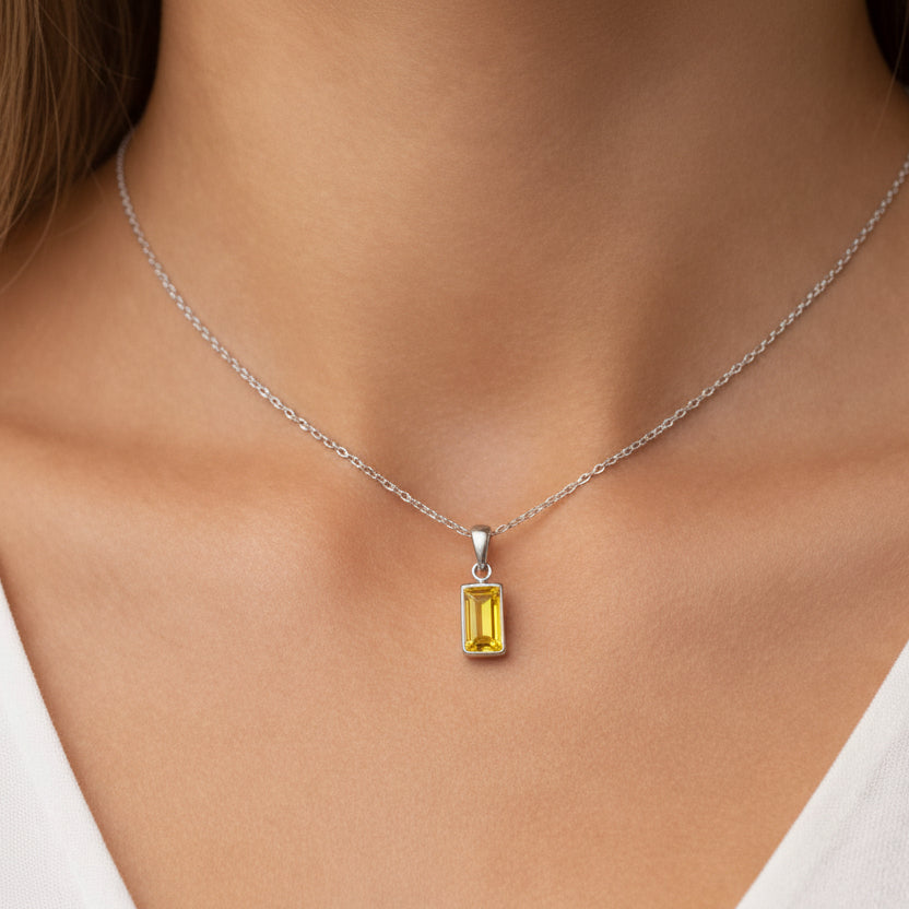 Necklace with a yellow gemstone pendant on a person wearing a white top.