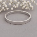 Silver band stacker ring on a grey surface with white flowers in the background