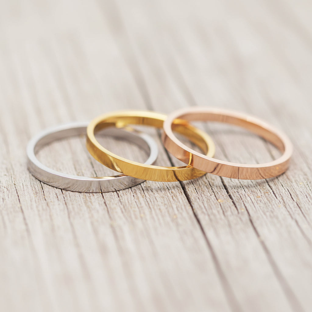 Three gold rings on a gray surface with blurred flowers in the background