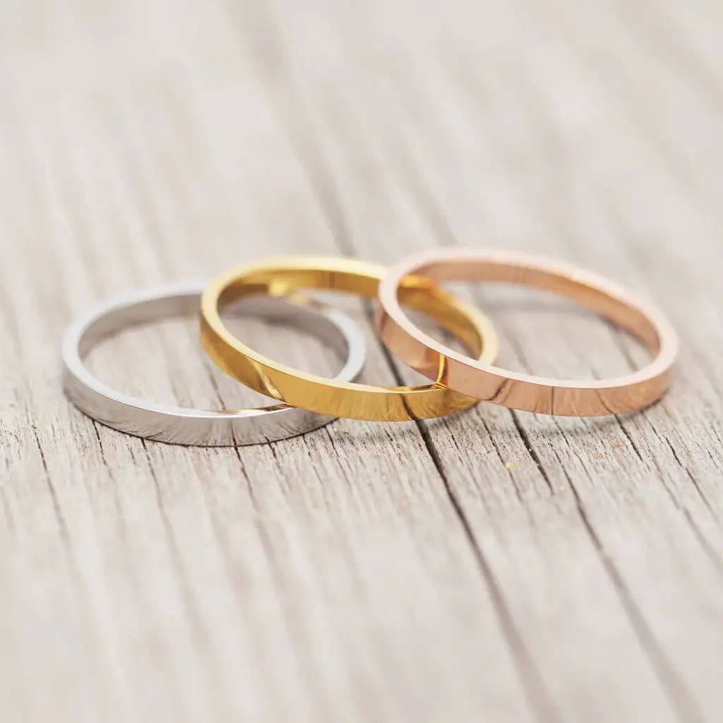 Three stackable band rings in silver, gold and rose gold on a light wooden surface