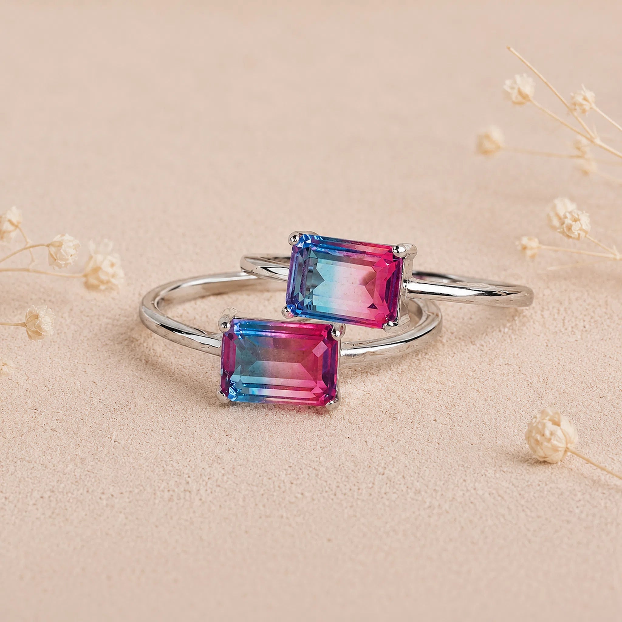 Two Sterling Silver Rings with an emerald cut Cotton Candy Tourmaline Gemstone with blue and pink colours on a soft light surface.