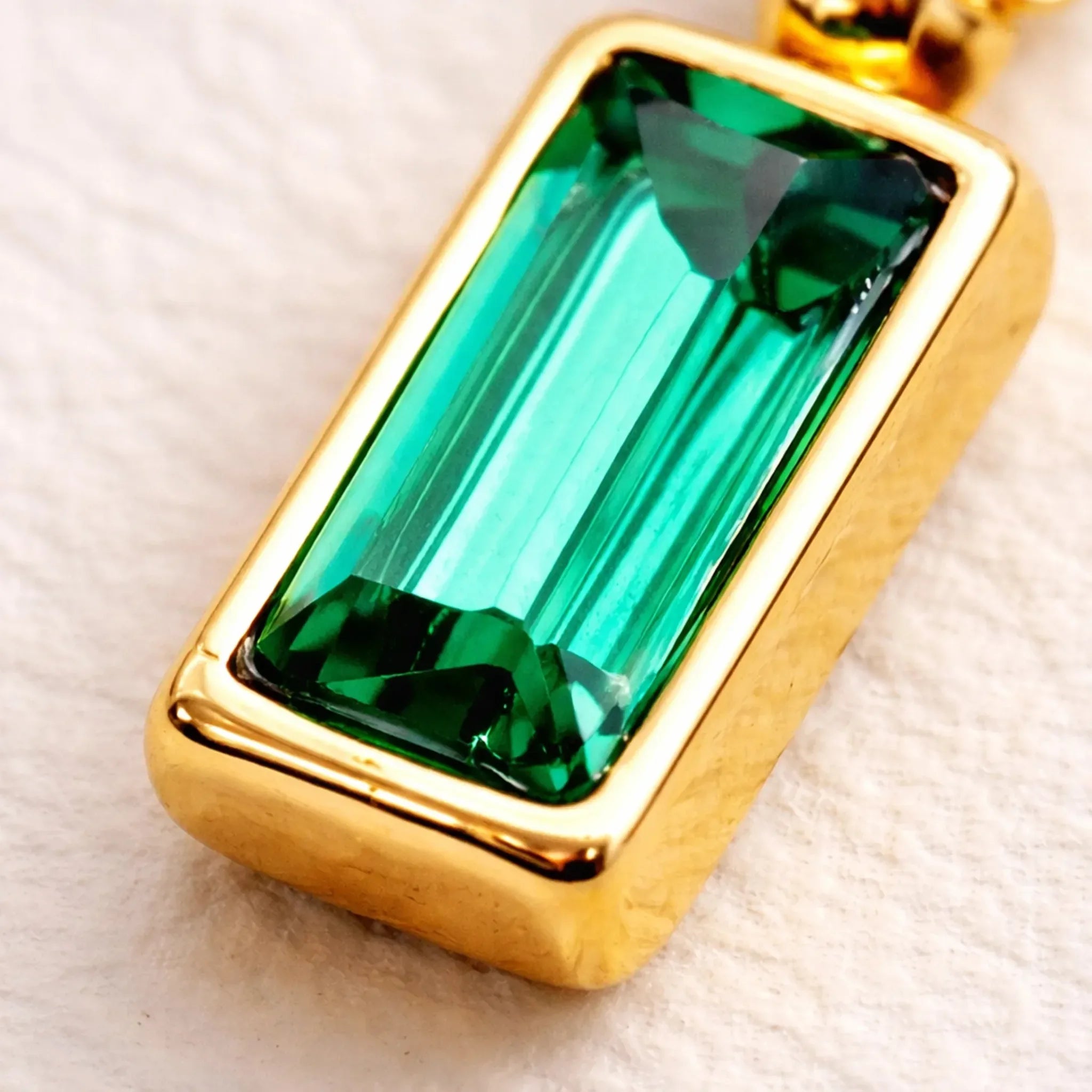 Gold pendant with a green gemstone on a light background