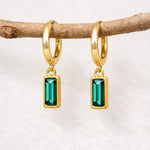 Gold hoop earrings with green gemstones hanging on a branch.