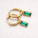 Gold hoop earrings with green gemstones on a gray background