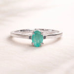 Sterling Silver ring with a oval solitaire claw set natural emerald gemstone on a light background