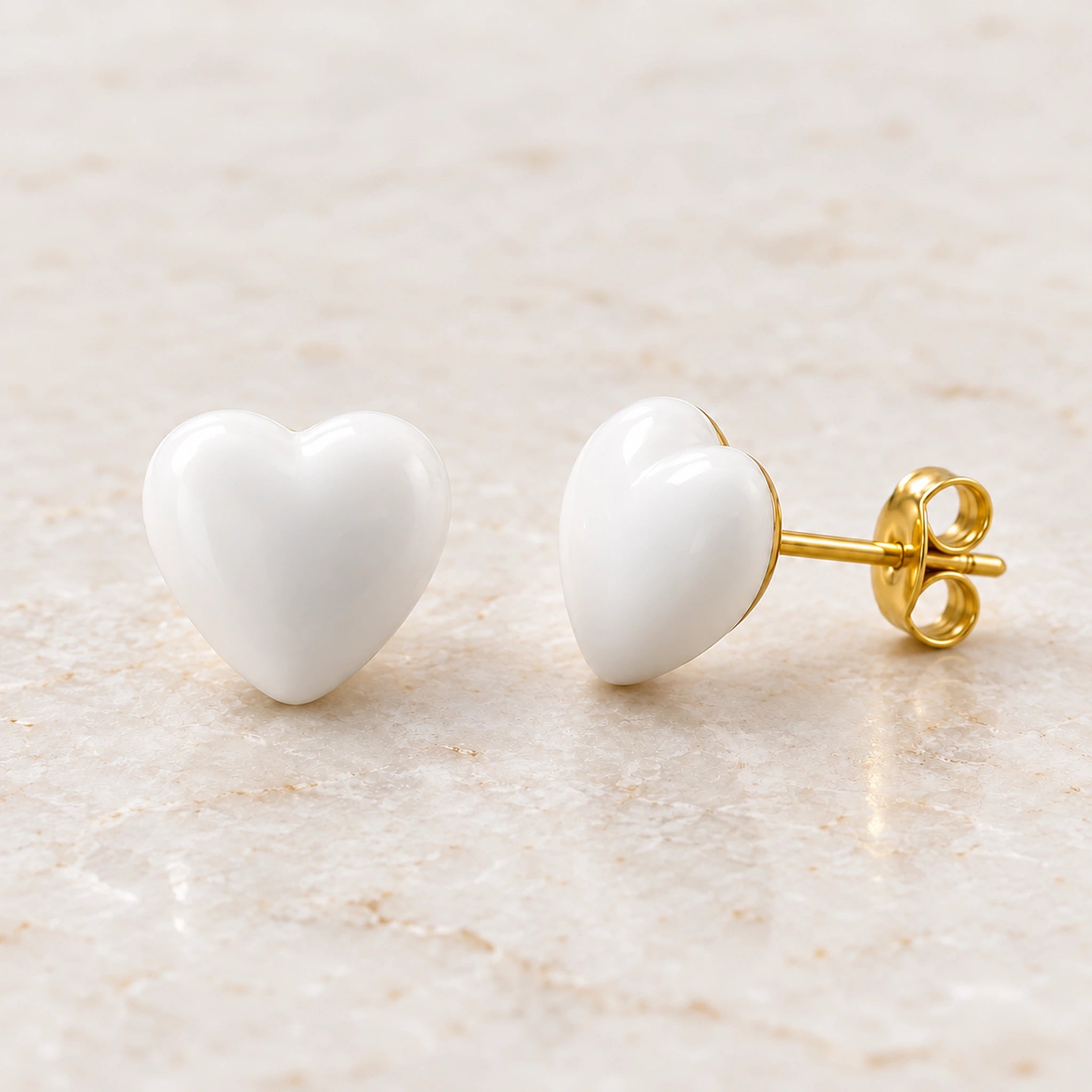 White epoxy heart stud earrings in gold PVD stainless steel, angle view