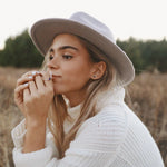 Woman wearing a beige hat and white sweater in a field