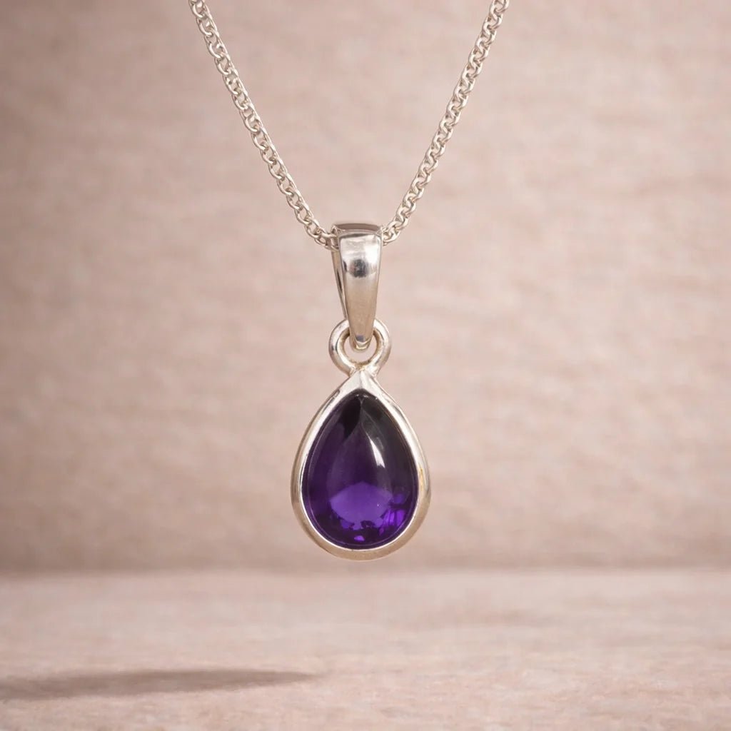 Sterling Silver pendant with a purple teardrop-shaped natural amethyst gemstone on a beige background