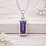 Silver waterproof necklace pendant with a purple gemstone on a wooden surface with white flowers.