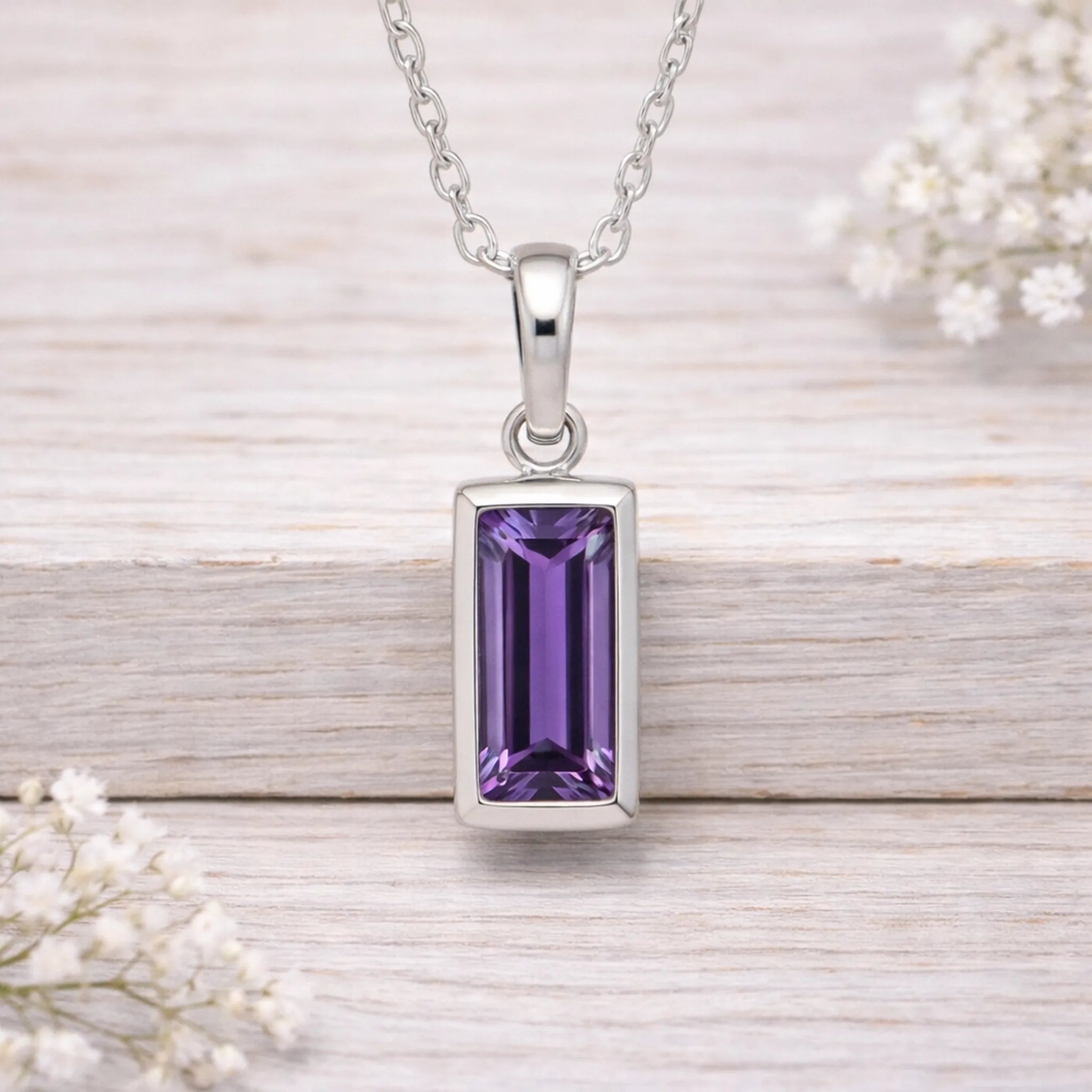 Silver waterproof necklace pendant with a purple gemstone on a wooden surface with white flowers.