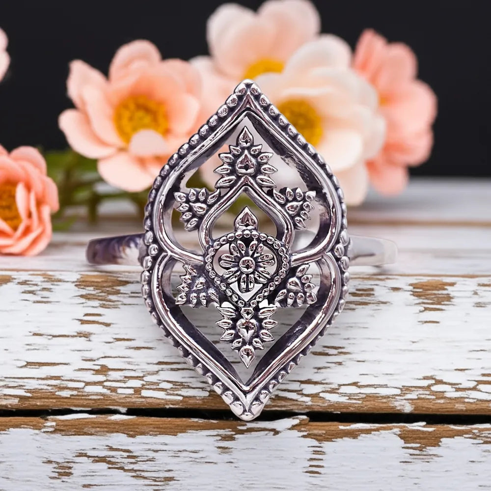 Decorative silver ring on a wooden surface with flowers in the background