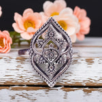 Decorative silver ring on a wooden surface with flowers in the background