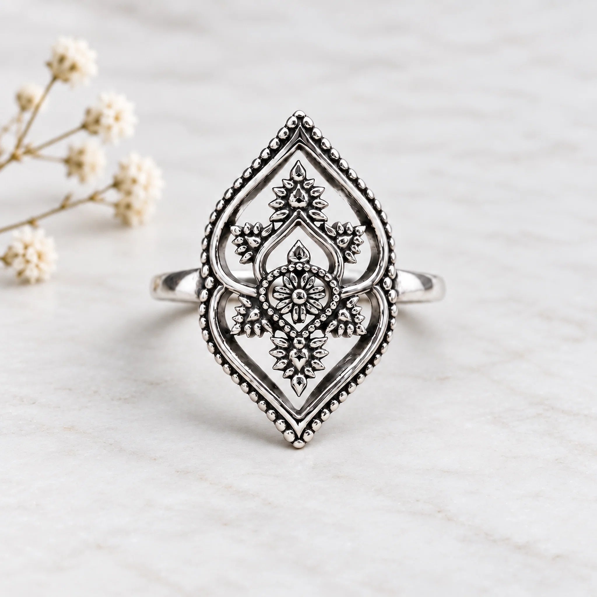 Decorative silver ring on a wooden surface with flowers in the background