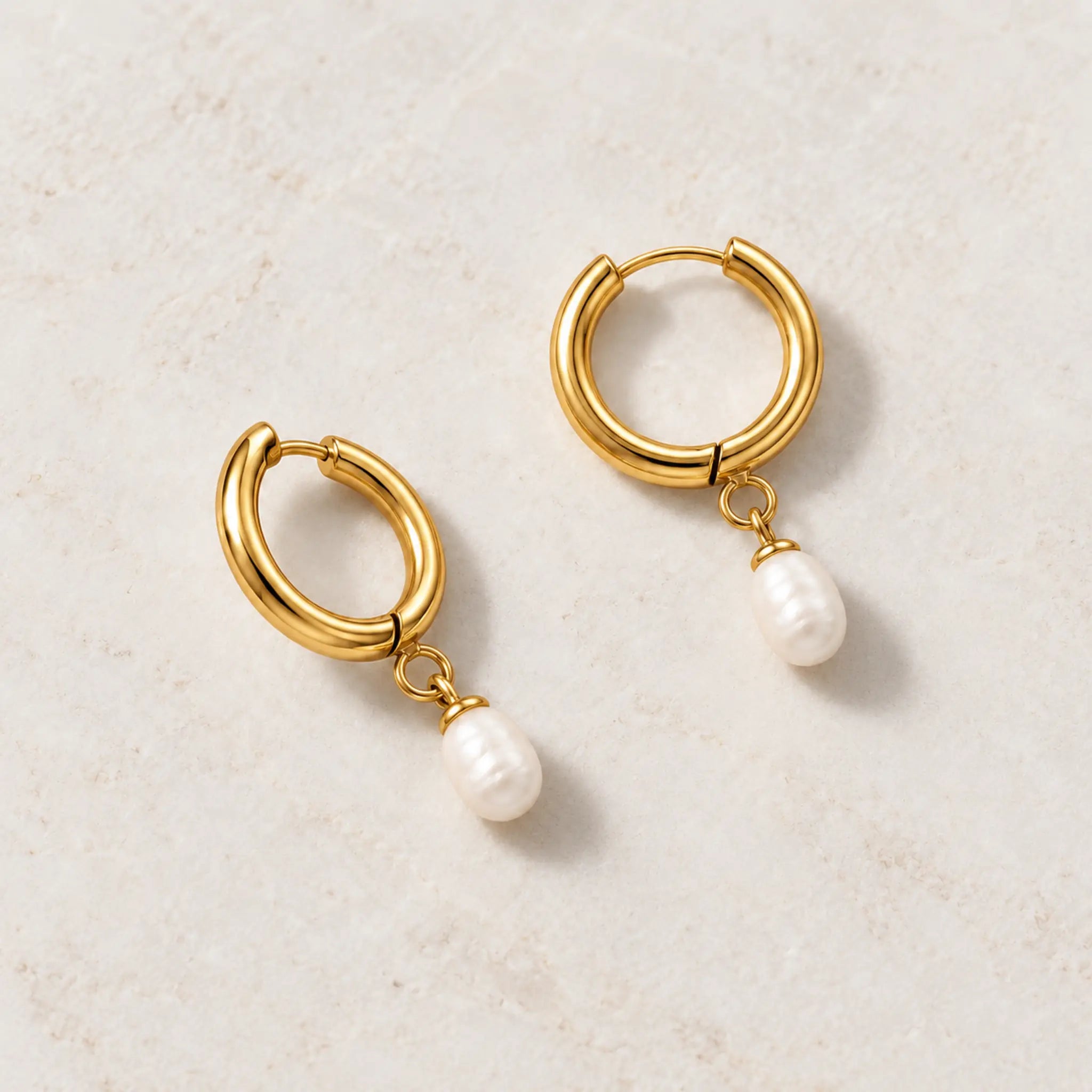 Freshwater pearl hoop earrings in gold PVD-plated stainless steel, pair resting on a light stone surface