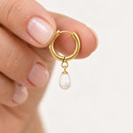 Freshwater pearl hoop earrings in gold PVD-plated stainless steel, single earring held between fingers