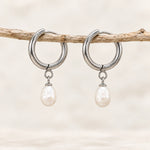 Freshwater pearl hoop earrings in silver PVD-plated stainless steel, pair hanging from a slender wooden branch