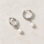 Freshwater pearl hoop earrings in silver PVD-plated stainless steel, pair resting on a light stone surface