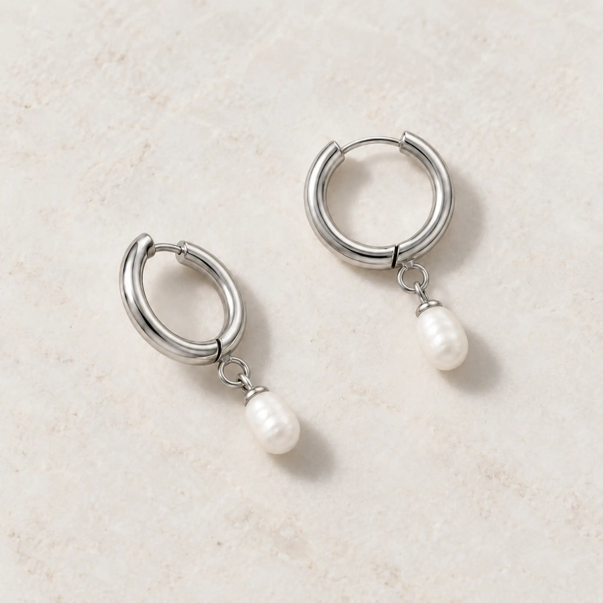 Freshwater pearl hoop earrings in silver PVD-plated stainless steel, pair resting on a light stone surface