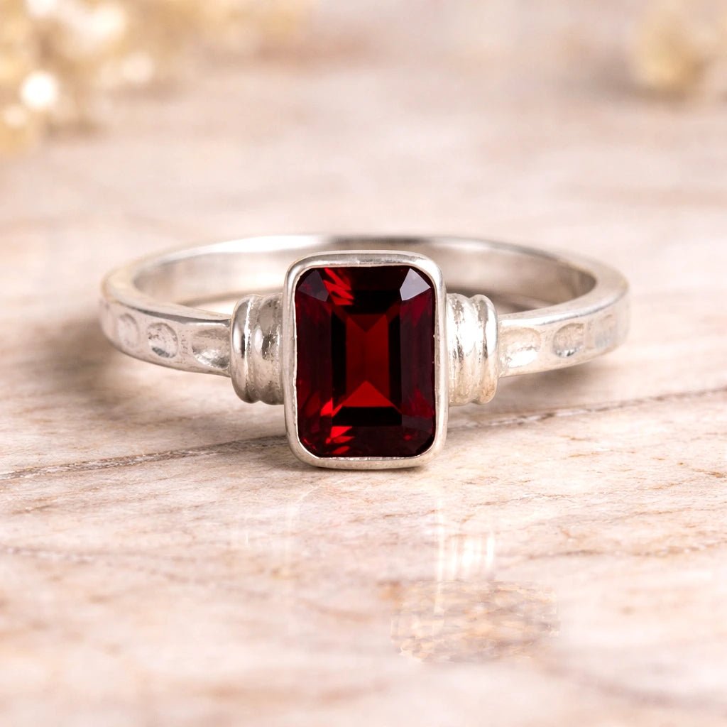 Silver ring with a red emerald cut natural garnet gemstone on a wooden surface