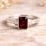 Silver ring with a red emerald cut natural garnet gemstone on a wooden surface
