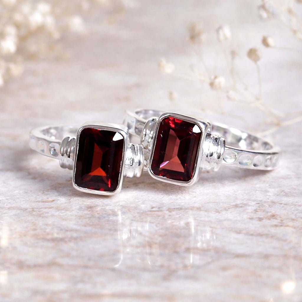 Silver rings with red garnet gemstones on a light wooden background