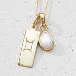 Gold necklace with gemini zodiac pendant and tear drop pearl pendant on a textured background