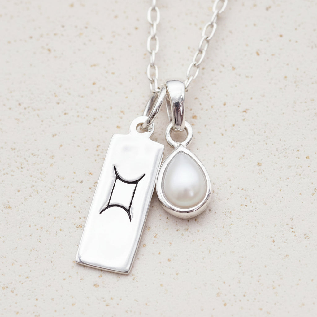silver necklace with Gemini zodiac pendant and tear drop pearl pendant on a natural background