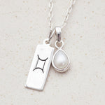 silver necklace with Gemini zodiac pendant and tear drop pearl pendant on a natural background