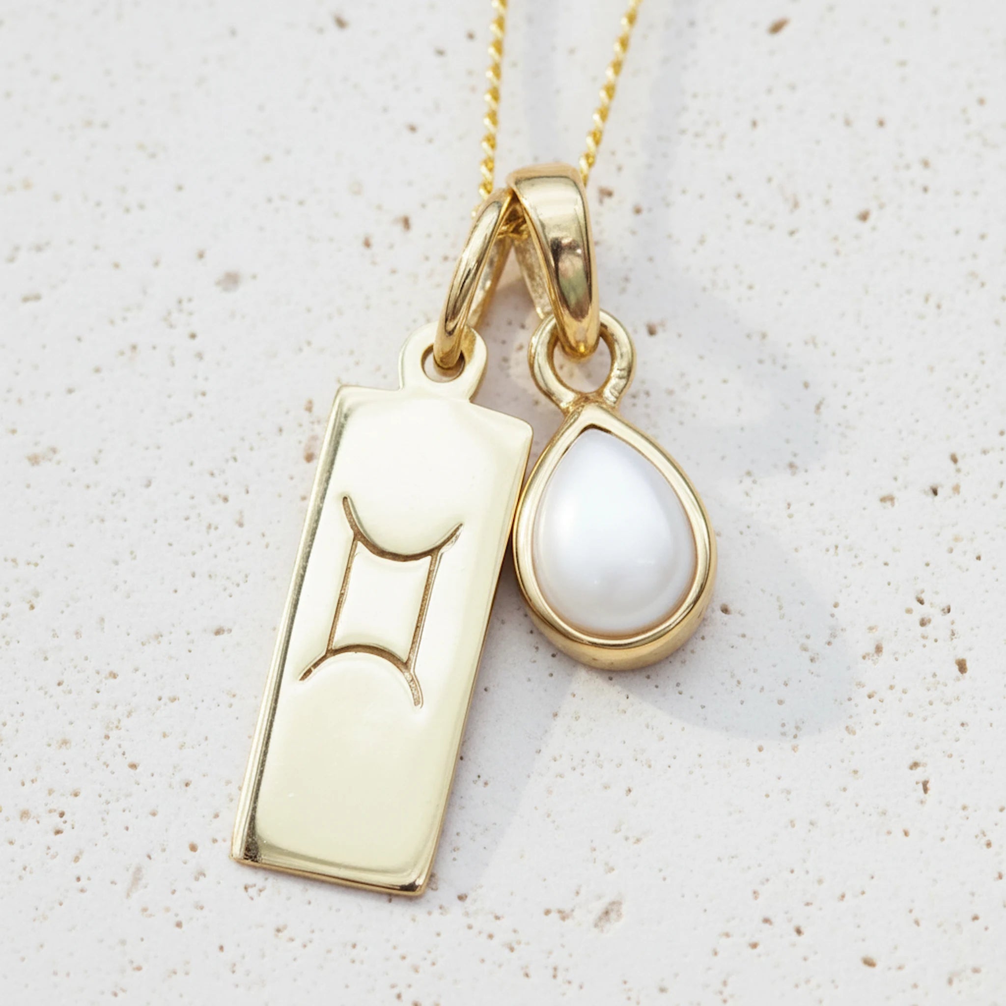Gold gemini zodiac pendant necklace with a june birthstone pearl pendant on a light background - personalised birthday jewellery gift