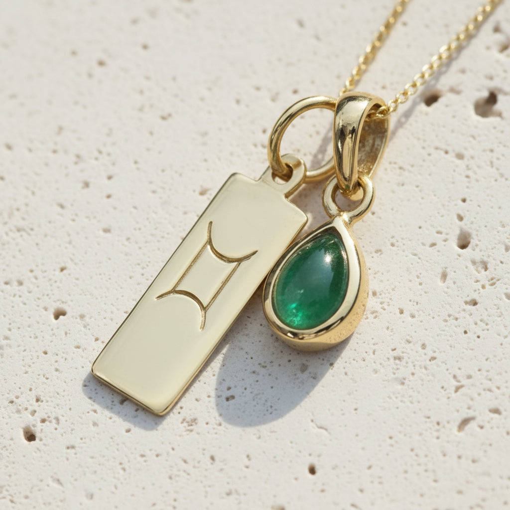 Gold necklace with a Gemini sign pendant and green emerald gemstone on a wooden surface